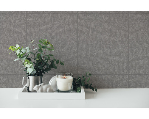 Dekoratives Arrangement mit gemusterter Tapete, Kerze und Grünpflanzen auf einem Tisch