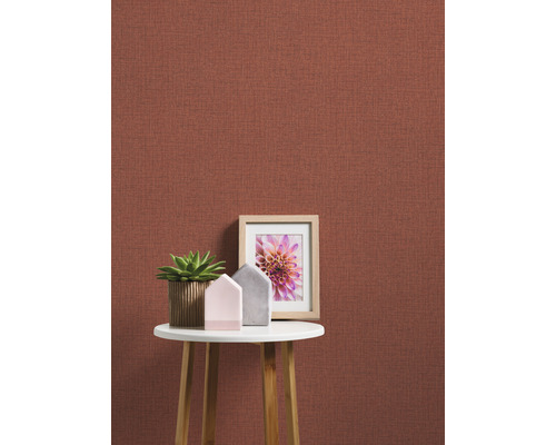 Nahaufnahme einer Wand mit Textiltapete, dekoriert mit einem Tisch, einer Zimmerpflanze und einem Bilderrahmen.