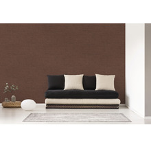 Wohnzimmer mit brauner Textiltapete, Futon und Kissen.