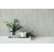 Scène décorative avec papier peint à motifs, bougie et eucalyptus sur un plateau.