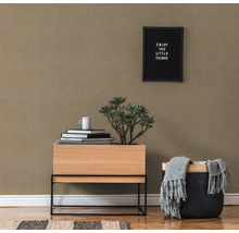 Nahaufnahme eines Raumes mit gemusterter Tapete, Holztisch mit Pflanze, Bücherstapel und Korb mit Decke