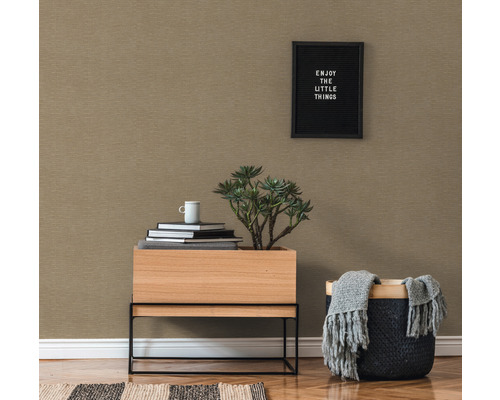 Nahaufnahme eines Raumes mit gemusterter Tapete, Holztisch mit Pflanze, Bücherstapel und Korb mit Decke