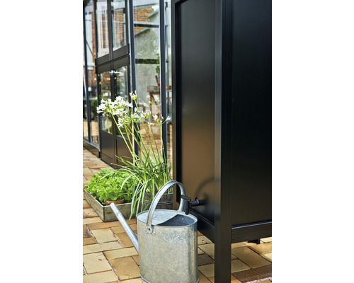 Récupérateur d''eau de pluie avec arrosoir et plantes devant une serre