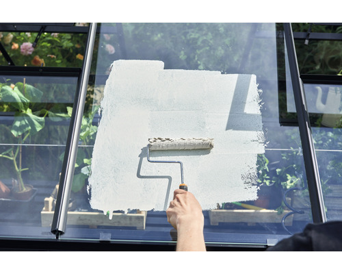 Eine Person streicht das Glas eines Gewächshauses mit einer Farbrolle.