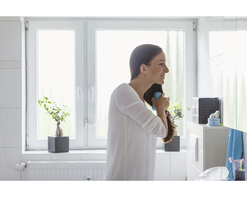 Frau bürstet Haare im hellen Badezimmer mit Fenster und Badezimmermöbeln