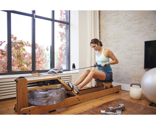 Frau benutzt Rudergerät in hellem Raum mit Sportgeräten.