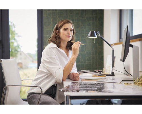 Femme assise à un bureau avec un ordinateur et une lampe de bureau.