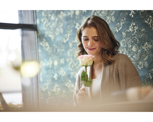 Frau hält Rose vor gemusterter Tapete