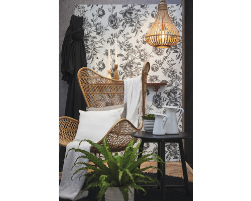 Dekoratives Wohnzimmer mit Rattansessel, Beistelltisch, Zimmerpflanzen und floraler Tapete