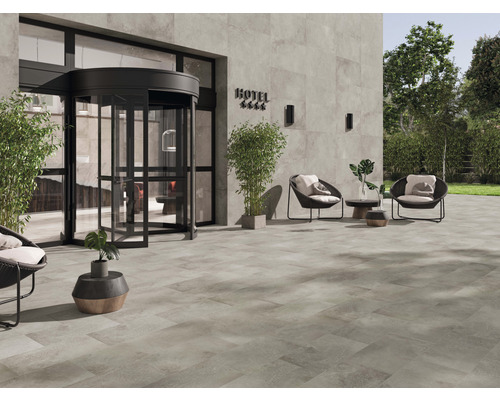 Espace extérieur avec carrelage au sol, entrée avec porte tambour et sièges devant un hôtel