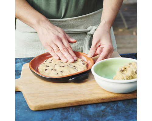 Eine Person drückt Teig in eine Backform auf einem Holzbrett.