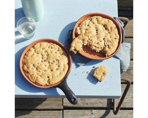 Zwei Schokoladenkekse in Pfannen auf einem Tisch, zusammen mit einer Wasserflasche und einem Glas Wasser.