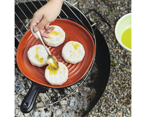 Camembert auf einer Grillpfanne wird mit einem Löffel beträufelt
