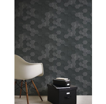 Raumansicht mit Wandgestaltung in dunkler Hexagon Optik, einem Stuhl und einer schwarzen Aufbewahrungsbox mit Büchern.