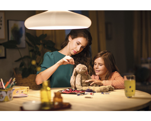 Une mère et sa fille sont assises à une table sous une lampe et réparent ensemble une peluche.