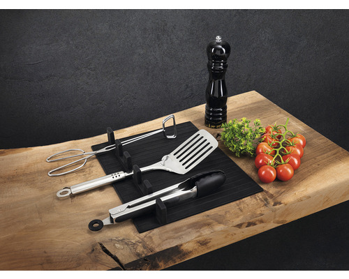 Grillbesteck, Grillwender, Grillzange, Pfeffermühle und Tomaten auf einem Holzbrett