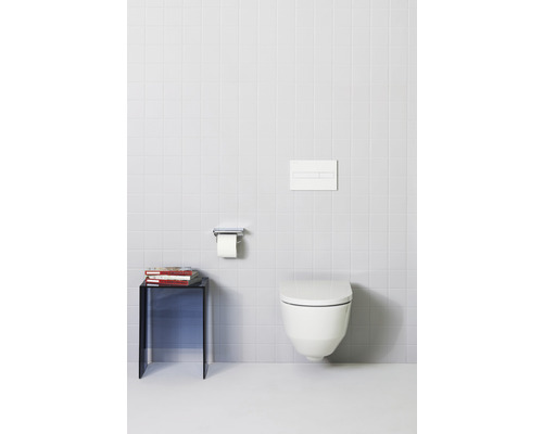 Salle de bains moderne avec WC suspendu, plaque de commande, porte-papier toilette et table d''appoint avec des livres.