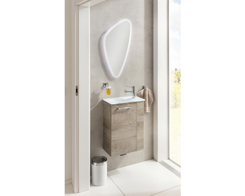 Salle de bains avec meuble sous-lavabo, miroir avec éclairage, distributeur de savon, serviette et poubelle.