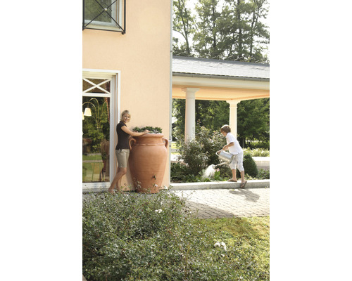 Frau an Regentonne in Amphorenform und Kind beim Giessen von Pflanzen im Garten