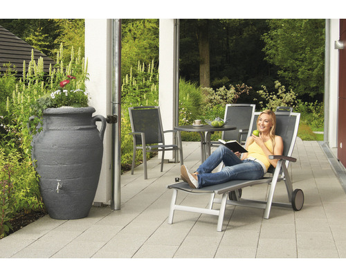 Dekorative Regentonne in Amphorenform mit Wasserhahn neben Terrasse mit Gartenmöbeln und entspannender Frau
