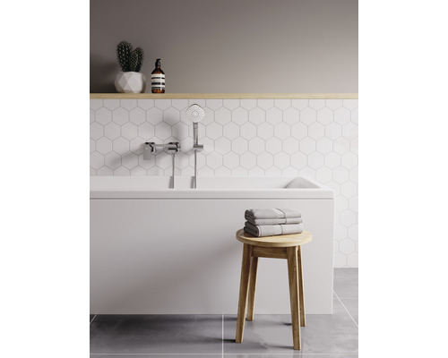 Salle de bains lumineuse avec baignoire, douchette, serviettes et tabouret en bois.