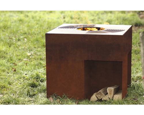 Quadratische Feuersäule aus Stahl mit Holzscheiten auf einer Rasenfläche.