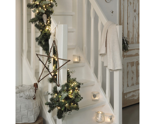 Escalier décoré avec une guirlande de sapin, des lumières, une étoile en bois et des photophores pour la période de Noël
