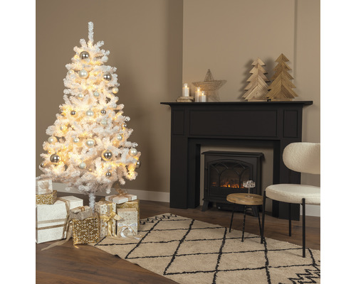 Weihnachtsbaum aus Kunstschnee mit Kugeln und Geschenken in einem Wohnzimmer mit Kamin