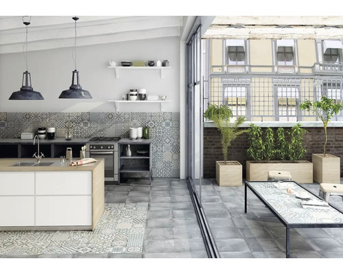 Cuisine claire avec îlot de cuisine, carrelage et accès à une terrasse avec bacs à plantes.