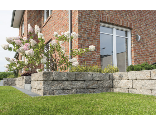 Außenaufnahme eines Gartens mit einer Trockenmauer aus Granitsteinen vor einem Haus mit Ziegelmauerwerk