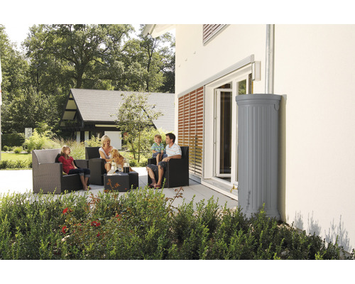Familie sitzt auf der Terrasse mit Regenwassertank zur Gartenbewässerung.