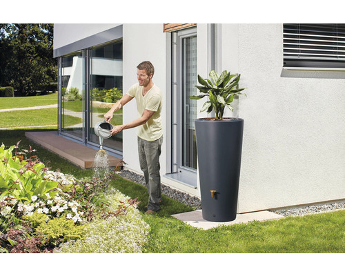 Un homme arrose des plantes dans le jardin avec un arrosoir, un réservoir d''eau de pluie à l''arrière-plan