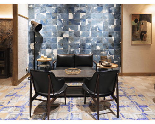 Salon avec carreaux à motifs bleus sur les murs et le sol, équipé de fauteuils, d''un canapé, de tables et d''un lampadaire.