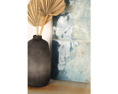Carreaux bleus décoratifs à côté d''un vase gris avec des feuilles de palmier séchées.