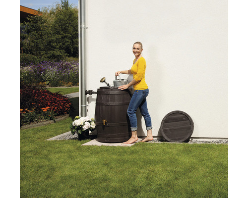 Frau befüllt Giesskanne an Regentonne im Garten