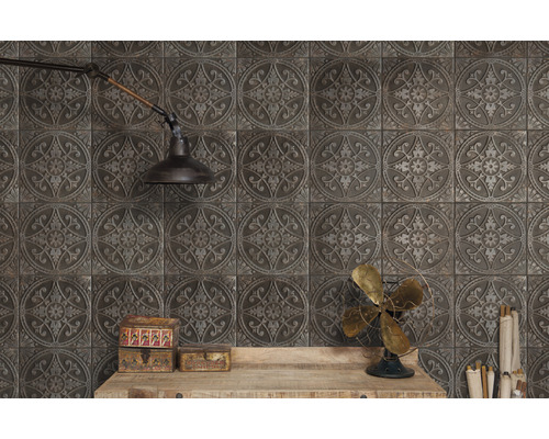 Wandgestaltung mit quadratischen Fliesen mit floralem Muster und rustikalem Flair, ergänzt durch eine Wandlampe und dekorative Elemente auf einem Holztisch.