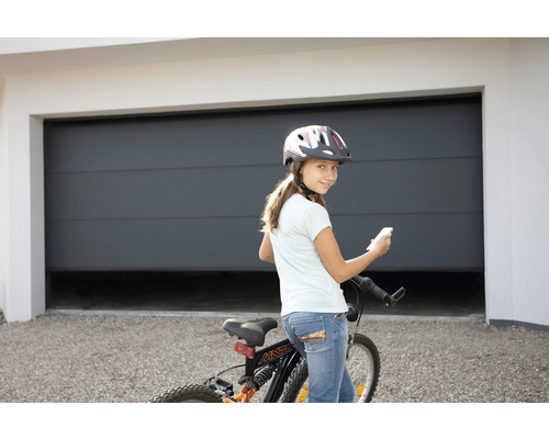 Fille avec vélo et casque devant un garage avec ouvre-porte de garage