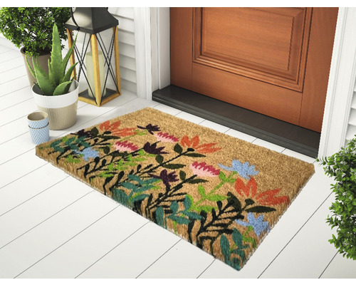 Paillasson en fibre de coco avec motif floral devant une porte d''entrée.