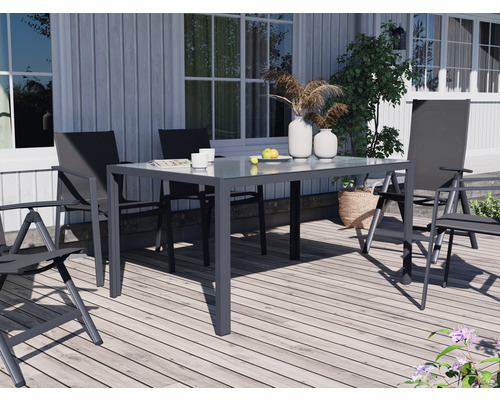 Gartenszene mit Esstisch und Stühlen auf einer Holzterrasse vor einem Haus.