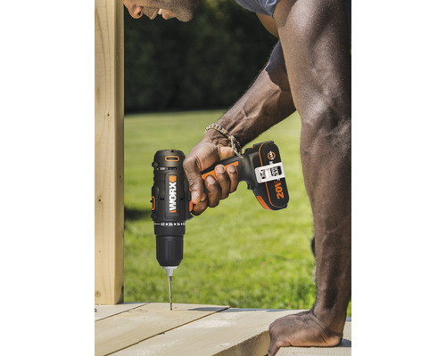 Un homme perce un trou dans une planche de bois avec une perceuse sans fil.