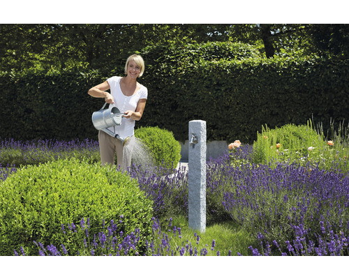 Frau giesst Pflanzen in einem Garten mit einem Wasserhahn aus Stein und Lavendel