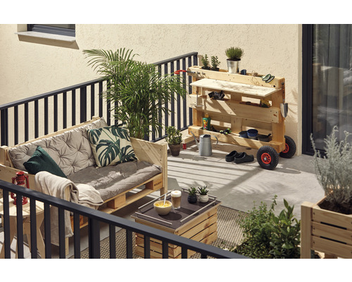 Balkon mit Holzmöbeln aus Paletten, darunter eine Couch mit Kissen, ein Tisch und eine mobile Werkbank mit Gartenutensilien.