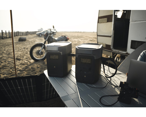 Scène avec deux générateurs électriques sur une table à l''extérieur avec une moto, une voiture et une caravane en arrière-plan.