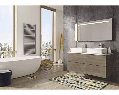 Salle de bain lumineuse avec baignoire, meuble sous-lavabo, miroir et sèche-serviettes.