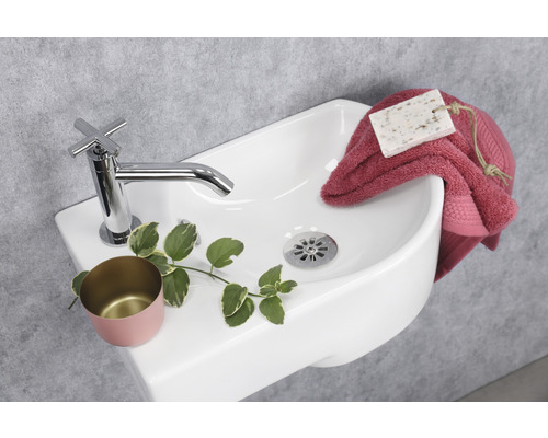 Detailansicht eines weißen Waschbeckens mit Armatur, Seife, Handtuch und Dekoration