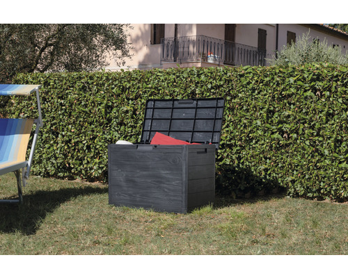 Coffre de jardin en plastique ouvert sur une pelouse devant une haie.