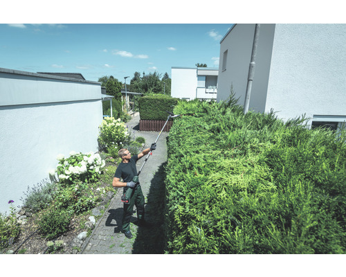 Un homme taille une haie avec un taille-haie à batterie dans le jardin
