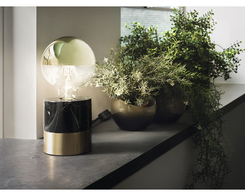 Lampe de table décorative avec une ampoule et une base en marbre et en métal, à côté de plantes artificielles