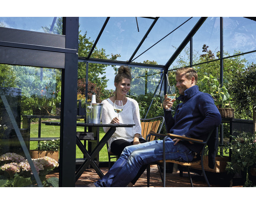Paar entspannt sich mit Wein in einem Gewächshaus mit Stahlrahmen und Glaswänden.