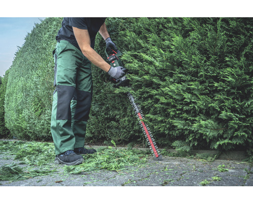 Une personne taille une haie avec un taille-haie sans fil.